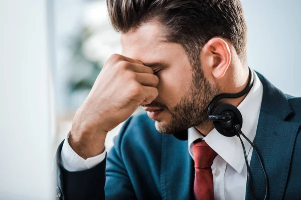 Empresário cansado em fone de ouvido com olhos fechados cobrindo rosto no escritório — Fotografia de Stock