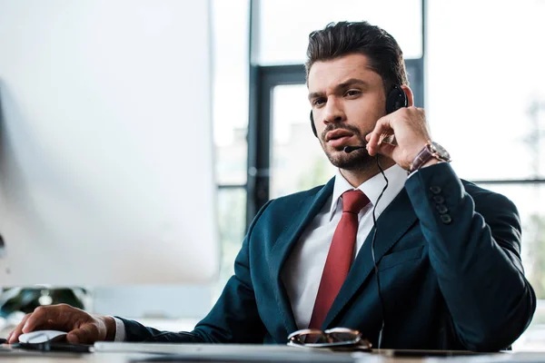 Guapo hombre de negocios tocando el micrófono mientras está sentado en la oficina - foto de stock