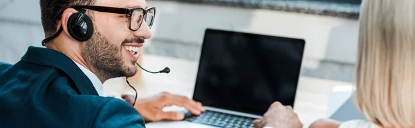 Colpo panoramico di uomo allegro in occhiali e auricolare guardando collega bionda in ufficio — Foto stock