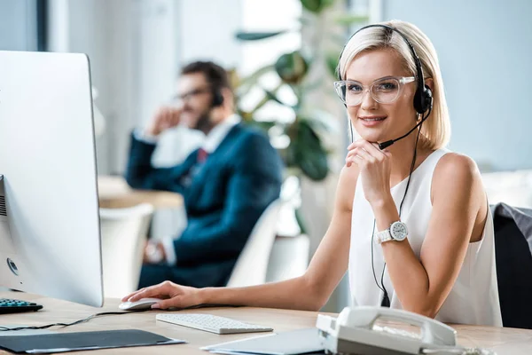 Enfoque selectivo de operador rubio alegre en auriculares mirando a la cámara - foto de stock