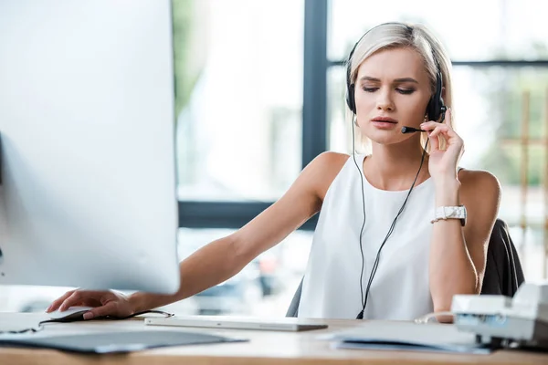 Messa a fuoco selettiva di bella donna bionda toccando auricolare e lavorando in ufficio — Foto stock