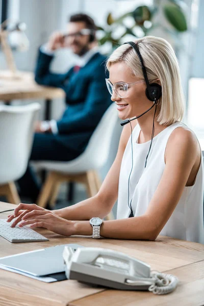 Selective focus of cheerful operator typing on computer keyboard near coworker — Stock Photo