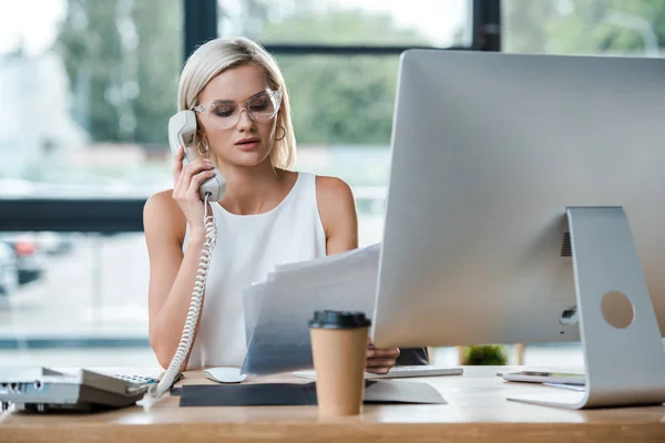 Messa a fuoco selettiva della donna d'affari guardando i documenti e parlando sul telefono retrò vicino tazza di carta — Foto stock