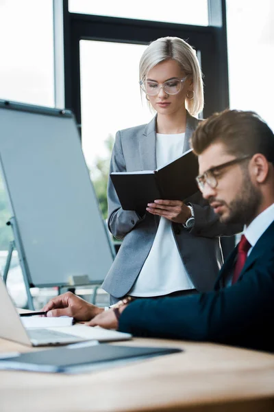 Messa a fuoco selettiva della donna attraente che tiene il taccuino vicino all'uomo usando il computer portatile — Foto stock