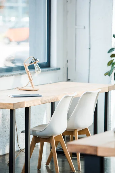 Selective focus of modern lamp on wooden table near chairs in office — Stock Photo