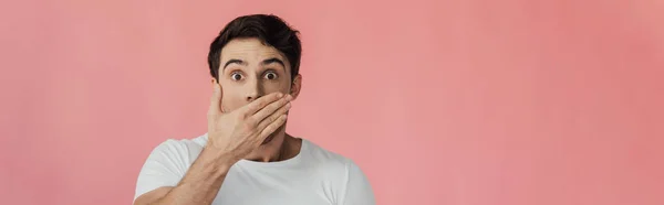 Plan panoramique de jeune homme effrayé couvrant la bouche avec la main et regardant la caméra isolée sur rose — Photo de stock