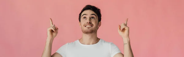 Panoramic shot of smiling man looking up and showing idea signs isolated on pink — Stock Photo