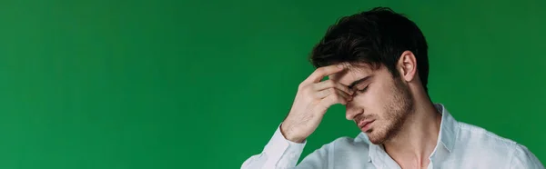 Panoramic shot of tired young man with closed eyes touching forehead isolated on green — Stock Photo