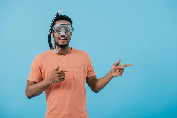 Hombre americano africano alegre en la máscara de buceo señalando con los dedos aislados en azul - foto de stock