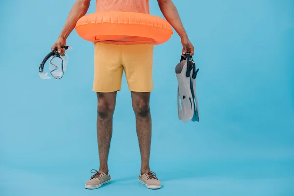 Vista recortada del hombre afroamericano sosteniendo aletas y máscara de buceo en azul - foto de stock