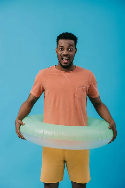 Hombre afroamericano emocionado de pie con anillo inflable aislado en azul - foto de stock