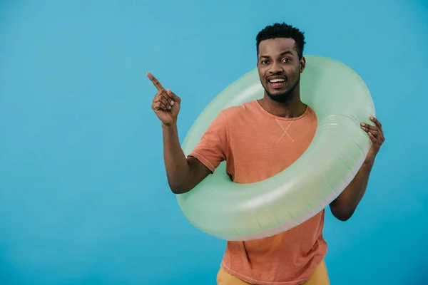 Homem americano africano positivo de pé com anel inflável e apontando com o dedo isolado no azul — Fotografia de Stock