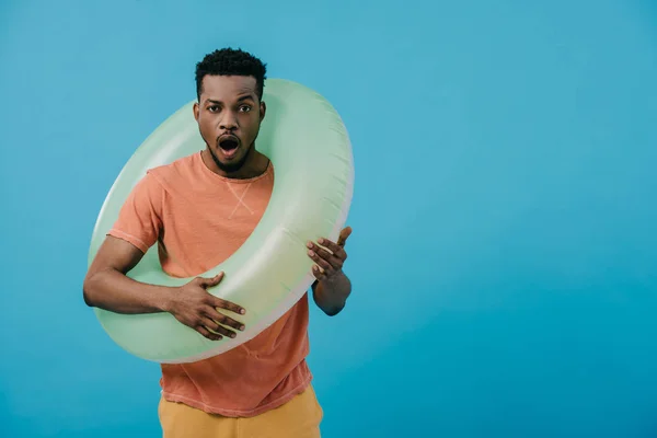 Sorprendido hombre afroamericano de pie con anillo inflable aislado en azul - foto de stock