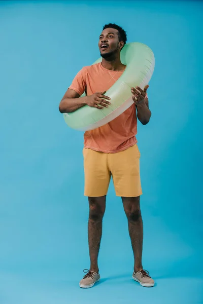 Sorpreso uomo afroamericano in piedi con anello di nuoto su blu — Stock Photo