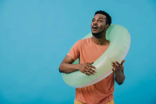 Surpris homme afro-américain debout avec anneau de natation isolé sur bleu — Photo de stock