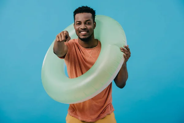 Foyer sélectif de l'homme afro-américain debout avec anneau de natation et pointant avec le doigt isolé sur bleu — Photo de stock