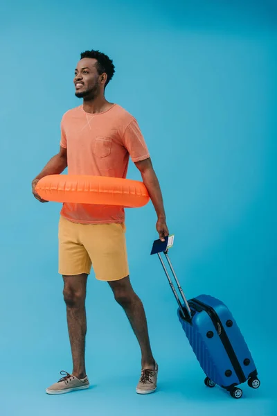 Happy african american tourist standing with passport and luggage on blue — Stock Photo