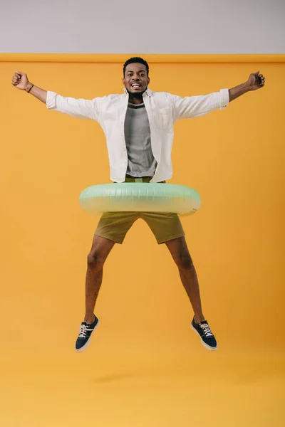 Hombre afroamericano feliz saltando con anillo de natación en naranja - foto de stock