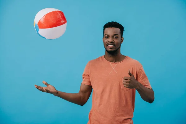 Homme afro-américain joyeux jetant ballon de plage dans l'air isolé sur bleu — Photo de stock