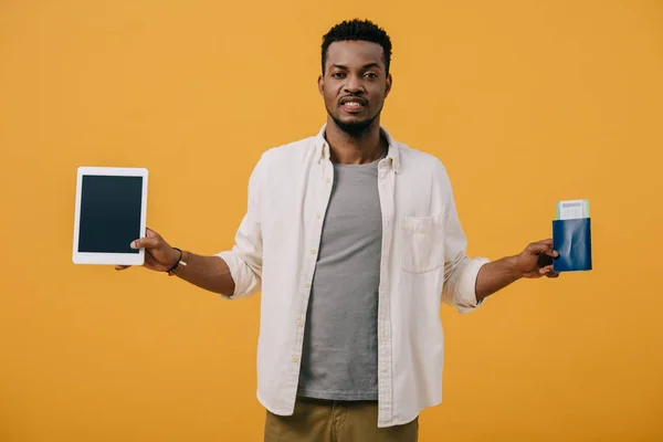 Homme afro-américain émotionnel tenant tablette numérique avec écran blanc et passeport isolé sur orange — Photo de stock