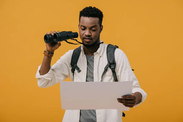 Frisé afro-américain homme tenant des jumelles et regardant papier blanc isolé sur orange — Photo de stock