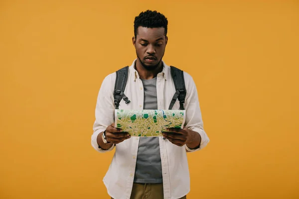 Schöner afrikanisch-amerikanischer Mann mit Rucksack, der isoliert auf orangefarbener Landkarte schaut — Stockfoto