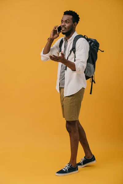 Lockiger afrikanisch-amerikanischer Mann, der auf einem Smartphone spricht, während er auf Orange steht — Stockfoto