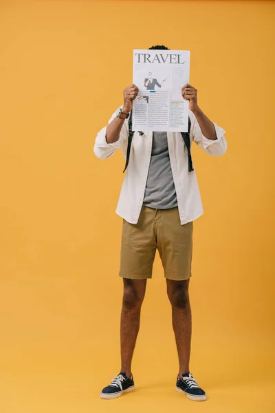 Homme afro-américain debout et couvrant le visage avec un journal de voyage sur jaune — Photo de stock
