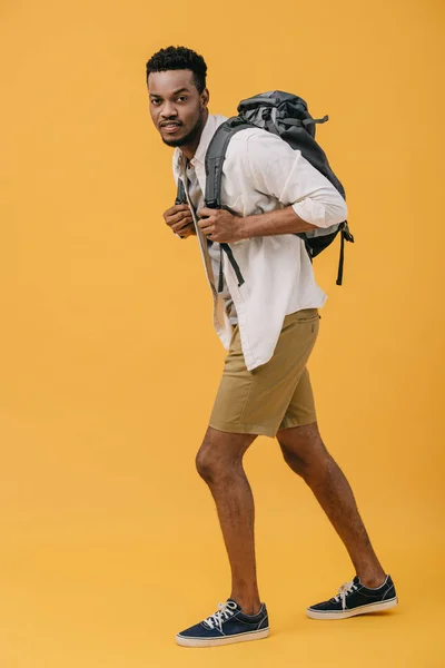 Handsome african american man walking with backpack on orange — Stock Photo