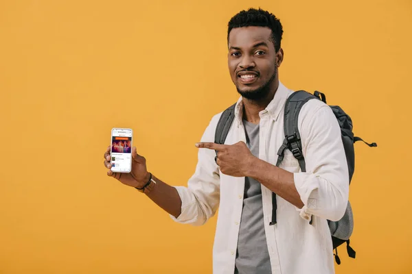 KYIV, UKRAINE - 27 JUIN 2019 : homme afro-américain joyeux pointant du doigt son smartphone avec application soundcloud à l'écran isolé sur orange — Photo de stock