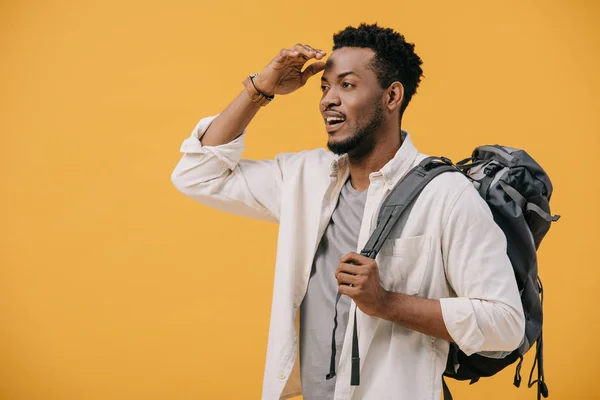 Handsome african american man gesturing while standing with backpack and searching isolated on orange — Stock Photo