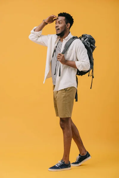 Щасливий афроамериканський чоловік жестикулює, стоячи з рюкзаком і шукаючи на апельсині — стокове фото