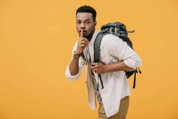 Africano americano hombre mostrando silencio signo mientras de pie con mochila aislado en naranja - foto de stock