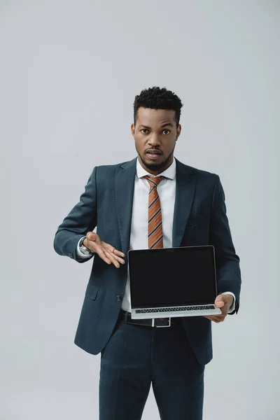 Handsome african american man gesturing while holding laptop with blank screen isolated on grey — Stock Photo