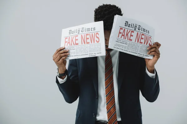 Homme d'affaires afro-américain couvrant le visage avec des journaux isolés sur gris — Photo de stock