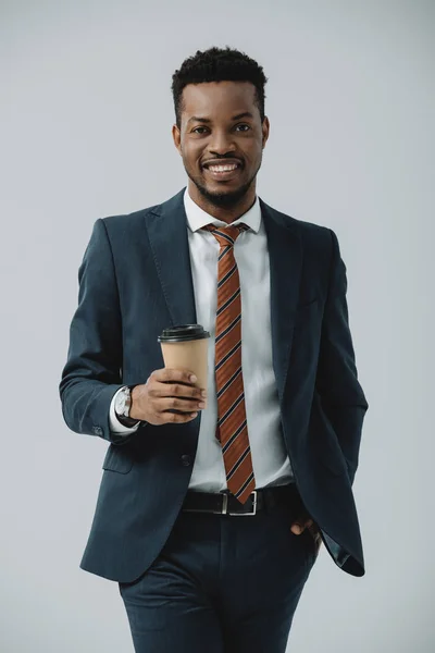 Alegre afroamericano hombre de negocios sosteniendo taza de papel aislado en gris - foto de stock