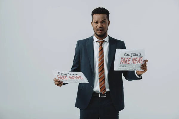 Empresario afro-americano emocional leyendo periódico con noticias falsas aisladas en gris - foto de stock