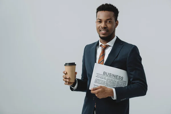 Веселий афроамериканський чоловік тримає ділову газету і паперовий стаканчик ізольовано на сірому — стокове фото