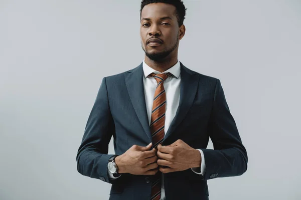 Schöner bärtiger afrikanisch-amerikanischer Geschäftsmann berührt Anzug isoliert auf grau — Stockfoto