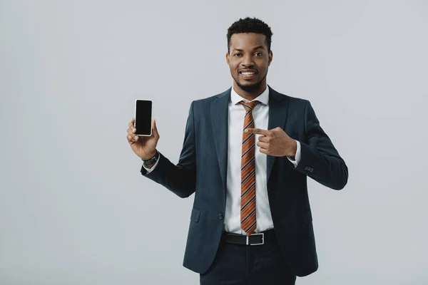Heureux homme d'affaires afro-américain pointant du doigt le smartphone avec écran vide isolé sur gris — Photo de stock