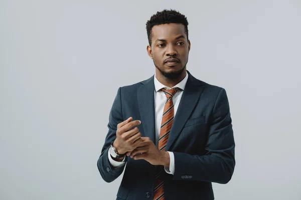 Bell'uomo d'affari afro-americano in giacca e cravatta toccare orologio isolato su grigio — Foto stock