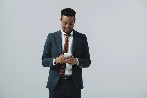 Heureux homme d'affaires afro-américain en utilisant smartphone isolé sur gris — Photo de stock