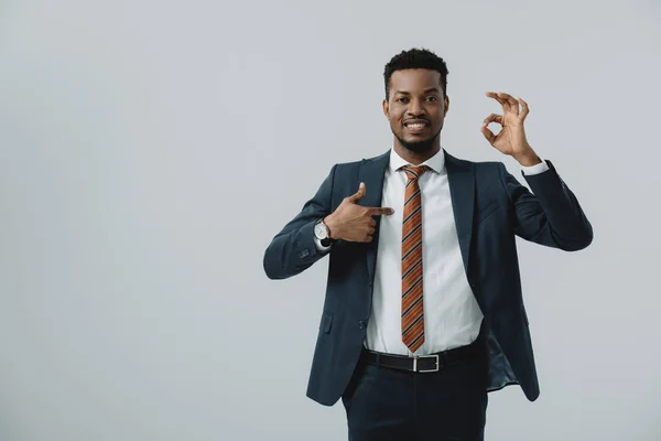 Hombre afroamericano feliz señalando con el dedo en el signo ok aislado en gris - foto de stock