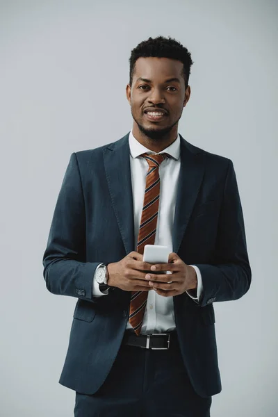 Homem afro-americano positivo em terno usando smartphone isolado em cinza — Fotografia de Stock