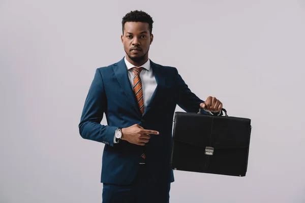 Афроамериканський чоловік вказує пальцем на портфелі ізольовано на сірому — стокове фото