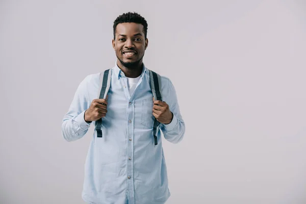 Glücklich afrikanisch-amerikanischer Mann steht und berührt Rucksack isoliert auf grau — Stockfoto