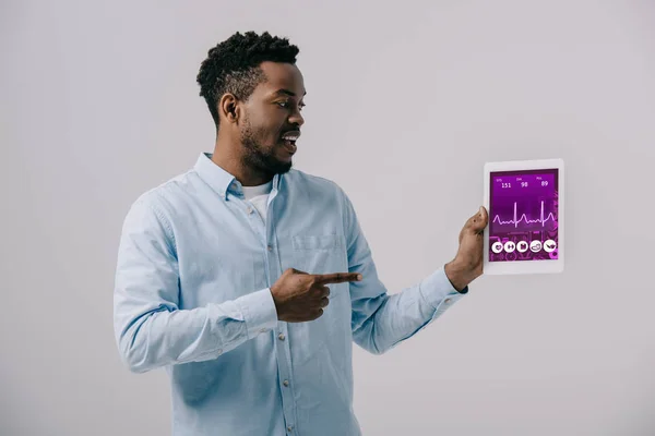 Happy african american man pointing with finger at digital tablet with medical app on screen isolated on grey — Stock Photo