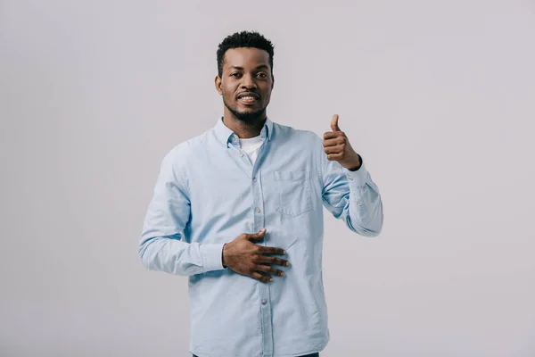 Cheerful african american man showing thumb up and touching stomach isolated on grey — Stock Photo