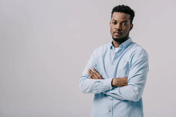 Bel homme afro-américain regardant la caméra et debout avec les bras croisés isolés sur gris — Photo de stock