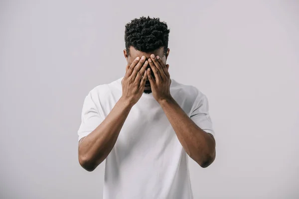 Homem americano africano em branco t-shirt cobrindo rosto com as mãos isoladas em cinza — Fotografia de Stock